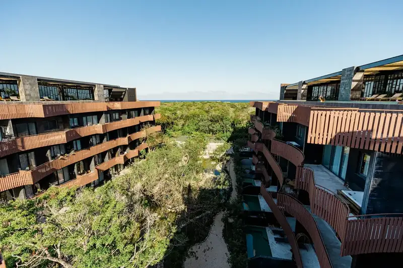 Amira District from above: two buildings with wooden balconies, jungle between them and the sea on the horizon