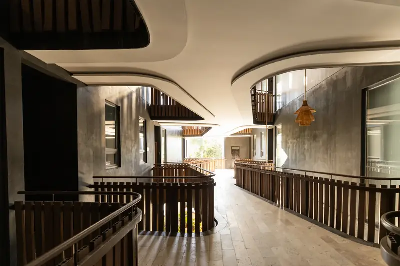 Open-air corridor with curved ceilings, wooden railings and a woven lamp