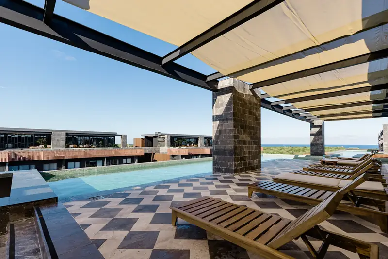 Rooftop pool with loungers under a shade sail, jungle and sea behind